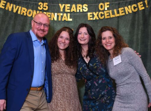 Group of formally dressed people standing in front of a green backdrop.