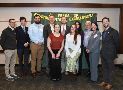 Group of formally dressed men and women posing for a photo in front of a green backdrop.