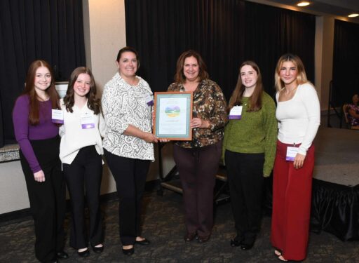 Formally dressed women standing in a group around an award.