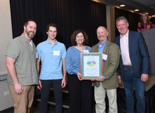 Five formally dressed people posing for a picture. A man and woman are in the middle holding an award.